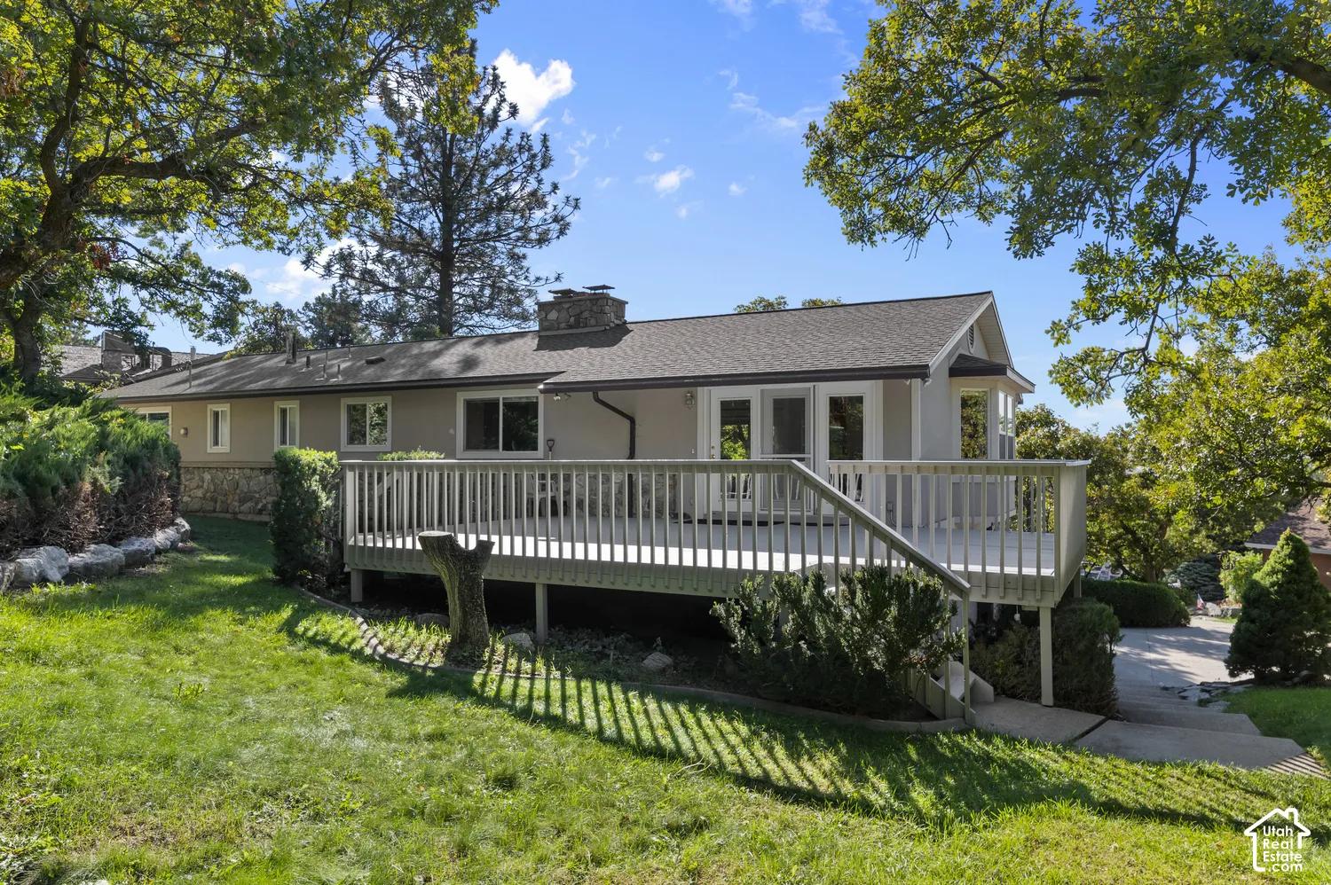 Expansive exterior deck with white railings, a stucco facade, stone accents, and multiple exterior doors