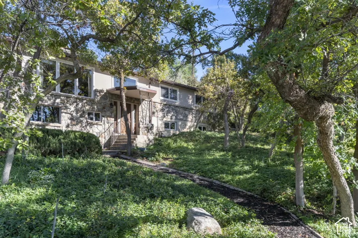 Stone exterior with stucco accents, mature trees, an entryway with steps and handrails, and a covered porch