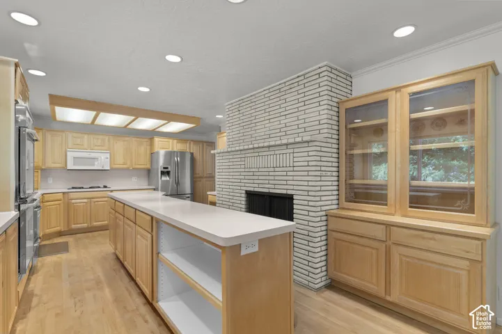 Natural wood cabinetry with integrated storage, white brick fireplace, center island with open shelving, stainless steel appliances, and recessed lighting