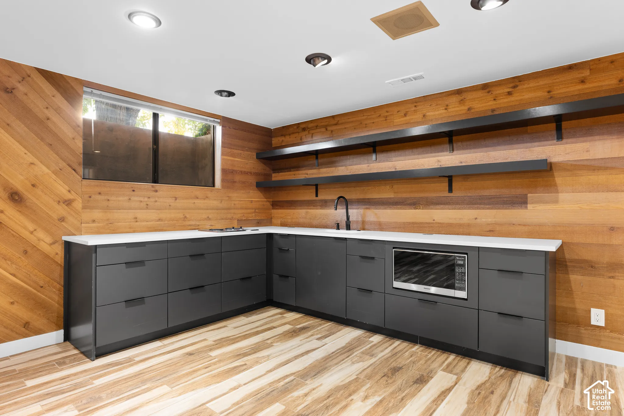 L-shaped lower cabinetry with integrated microwave, white solid surface countertops, a matte black faucet, and wood-finish flooring