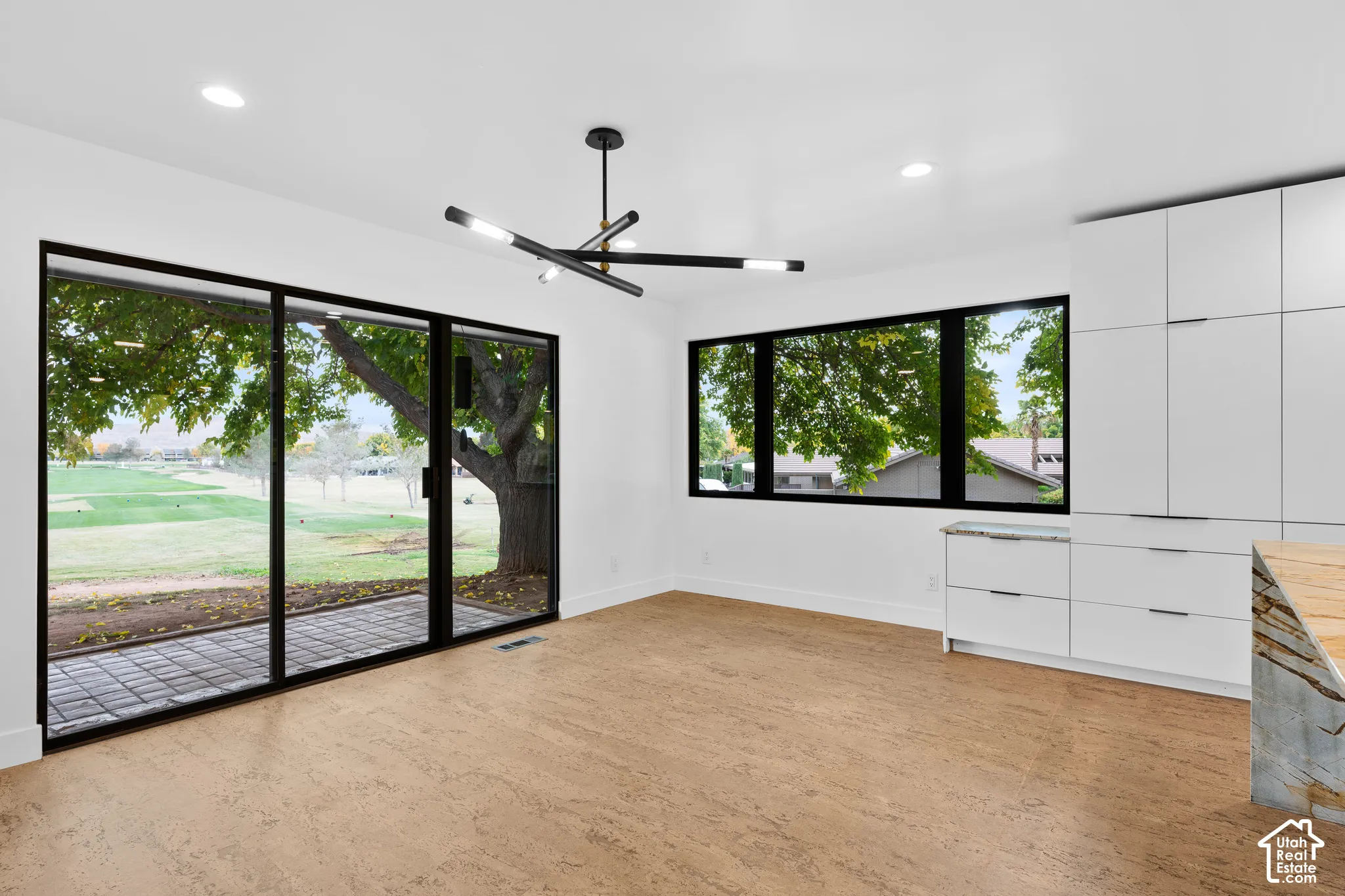 White walls, modern black and gold chandelier, wood-finish flooring, full-height white cabinetry with integrated pulls, and a stone slab countertop