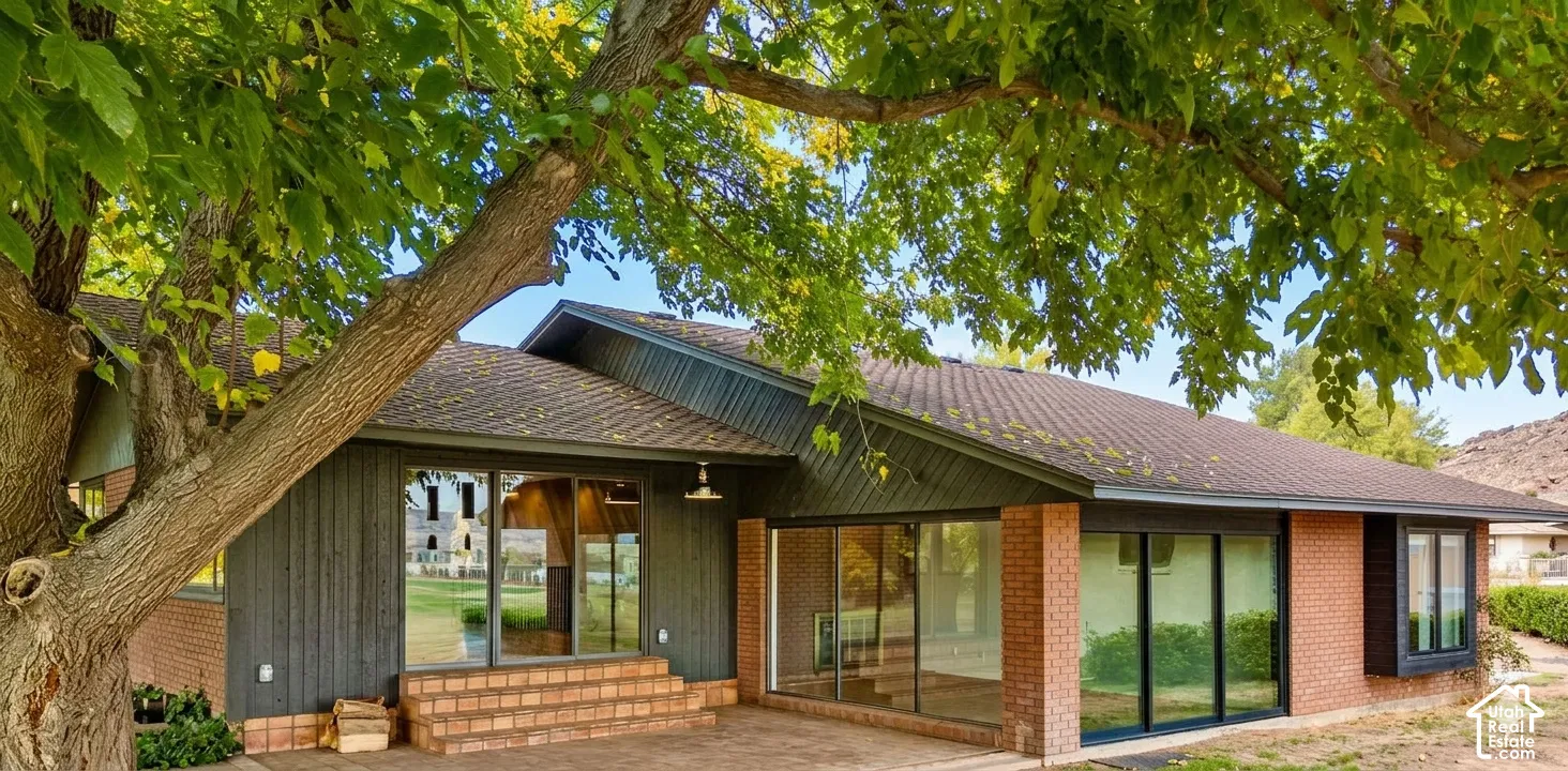 Brick and vertical siding exterior with extensive window placements, a patio, and mature trees