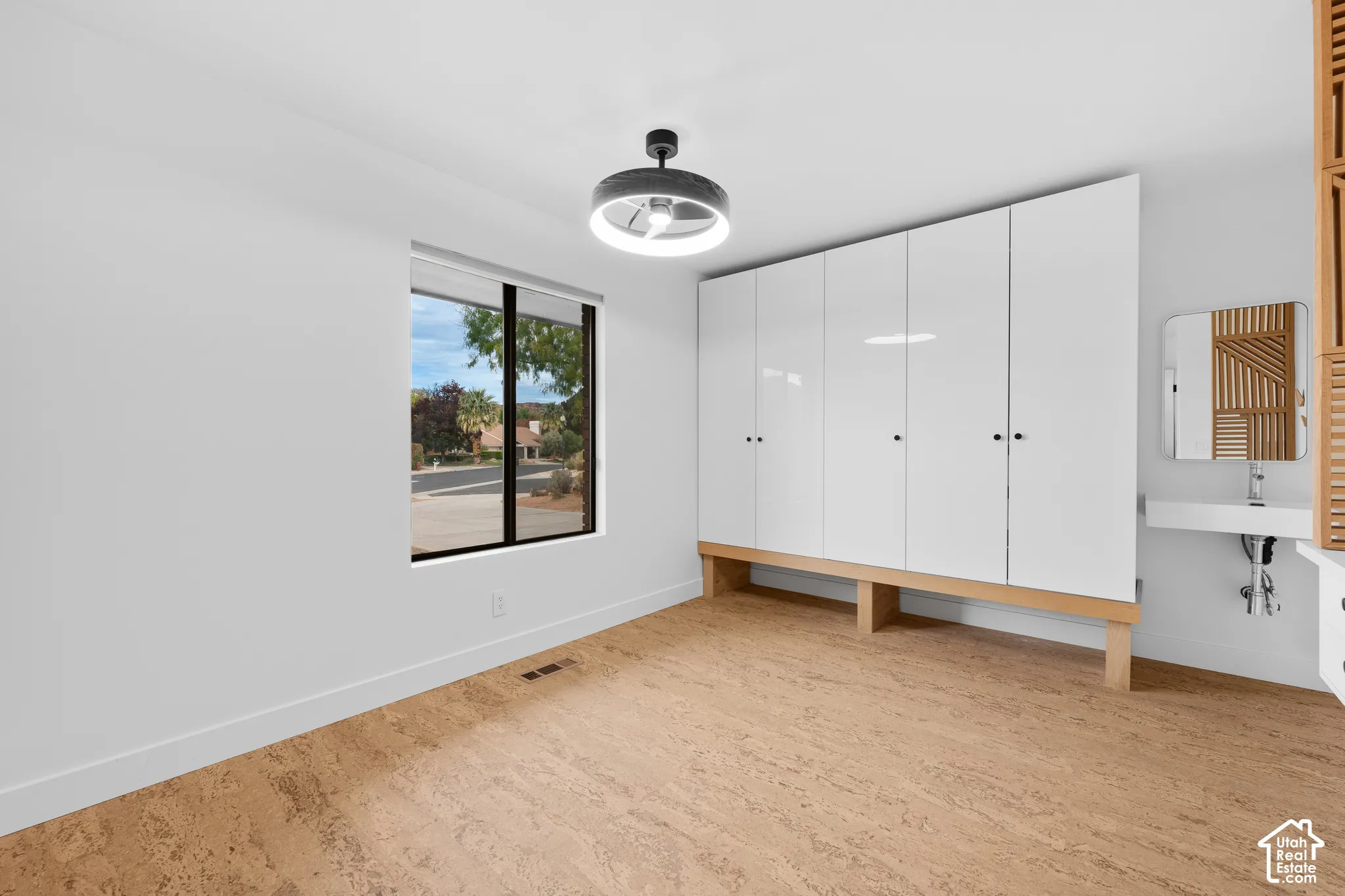 Bright interior with a large window, cork flooring, built-in white cabinetry, and a wall-mounted sink with a mirror