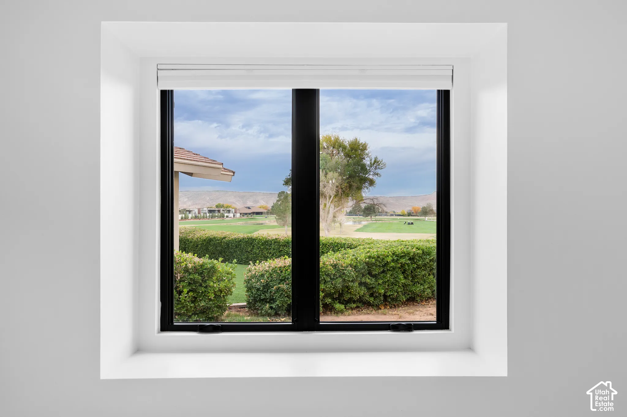 White-trimmed window with black frames overlooking a manicured golf course, distant mountains, and a clear sky