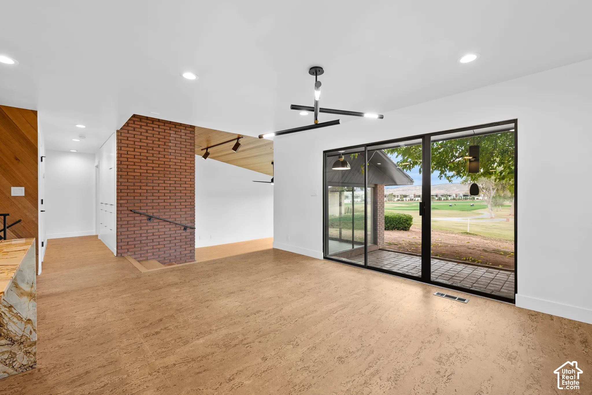 Wood-finish flooring, exposed brick wall, contemporary lighting fixture, full-height sliding glass doors, and a patio with a tiled surface