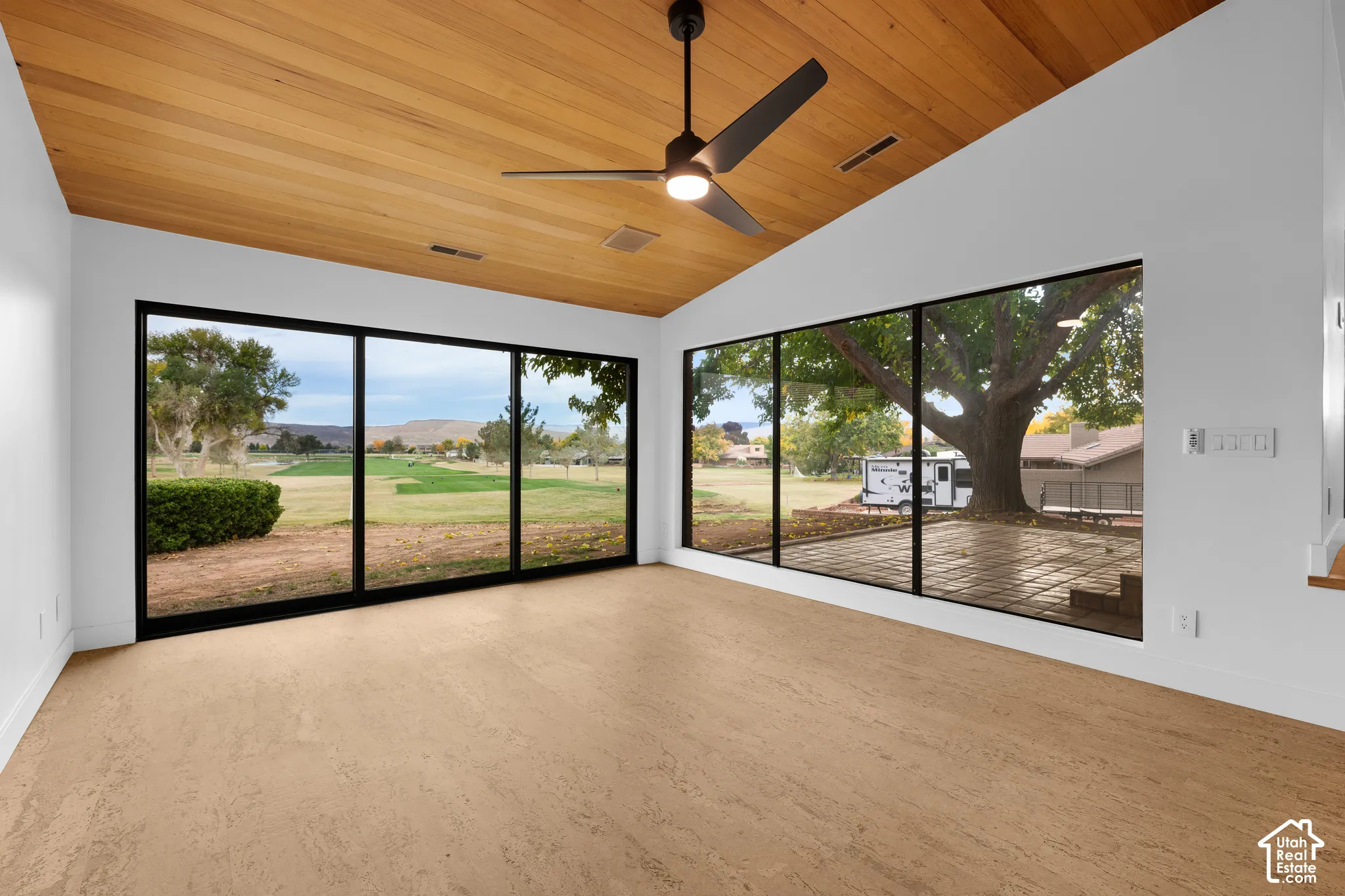 Angled wood-panel ceiling, large black-framed windows, and light-toned flooring