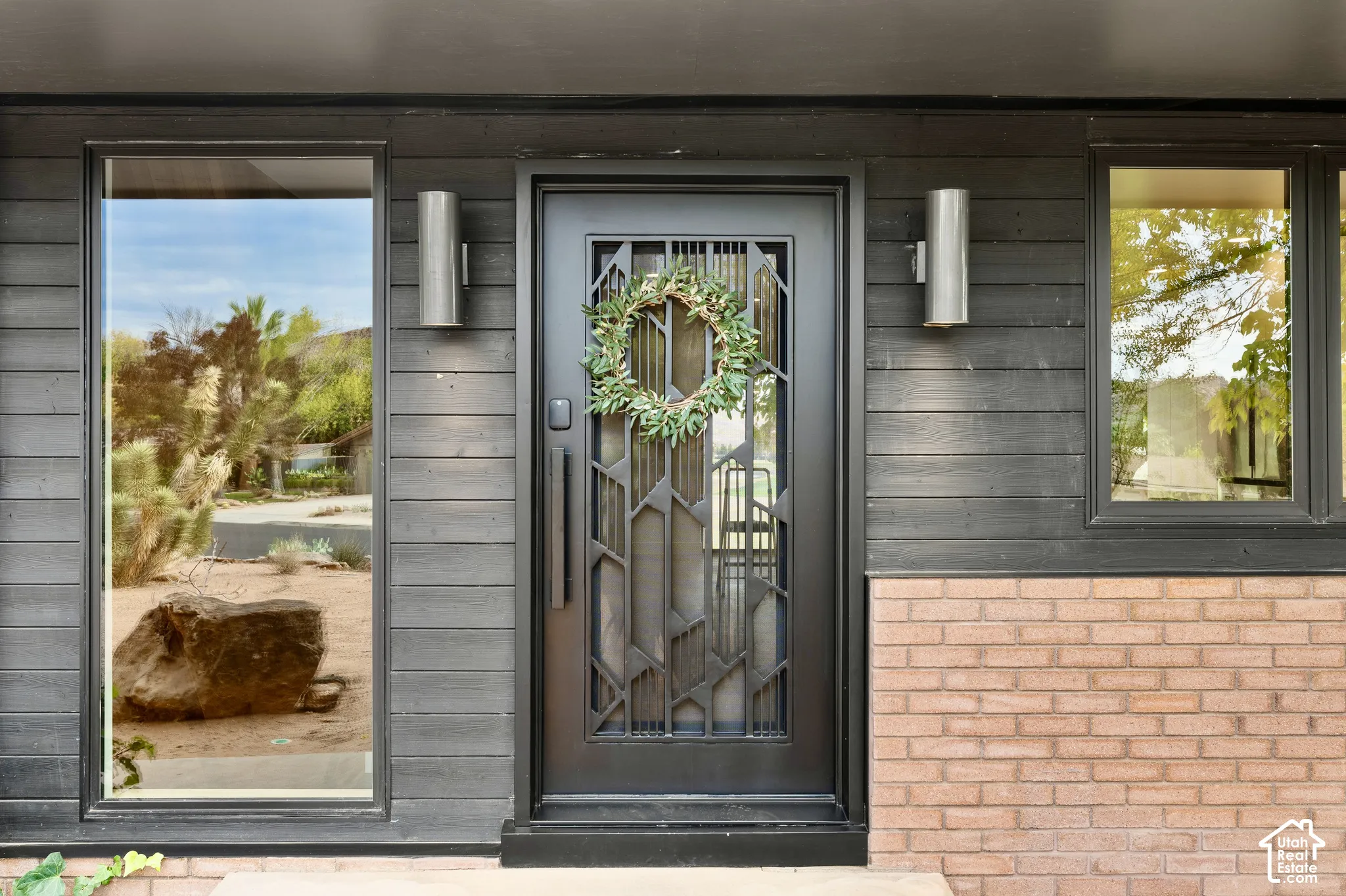 Horizontal wood siding, brick façade, metal entry door with decorative glass, and dual exterior sconce lighting