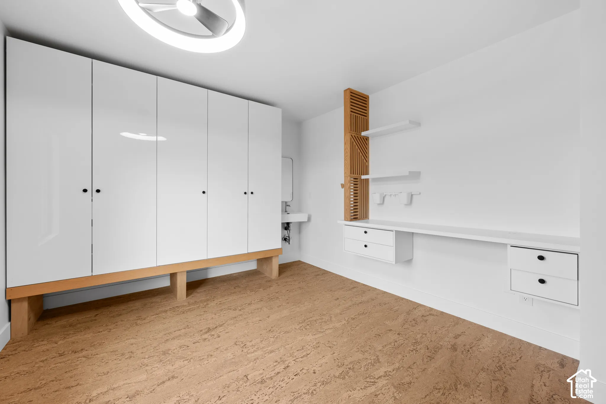 White high-gloss cabinetry with wood-finish base, cork flooring, and a modern ceiling light fixture