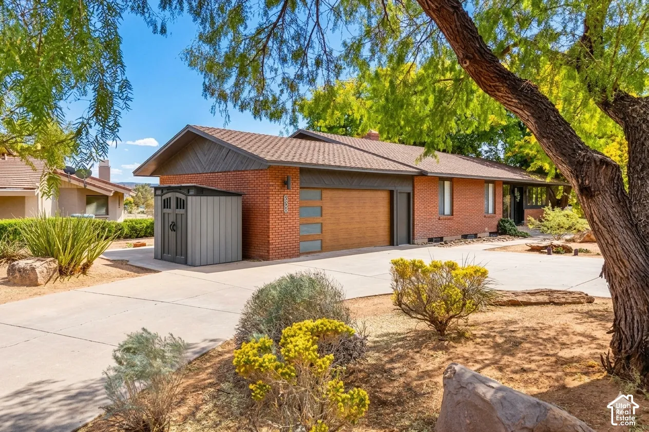 Brick exterior with a brown shingle roof, wood-look garage door, and mature landscaping
