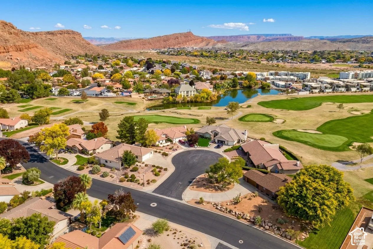 Aerial perspective showcasing a residential community with golf course greens, a pond, and surrounding desert landscape