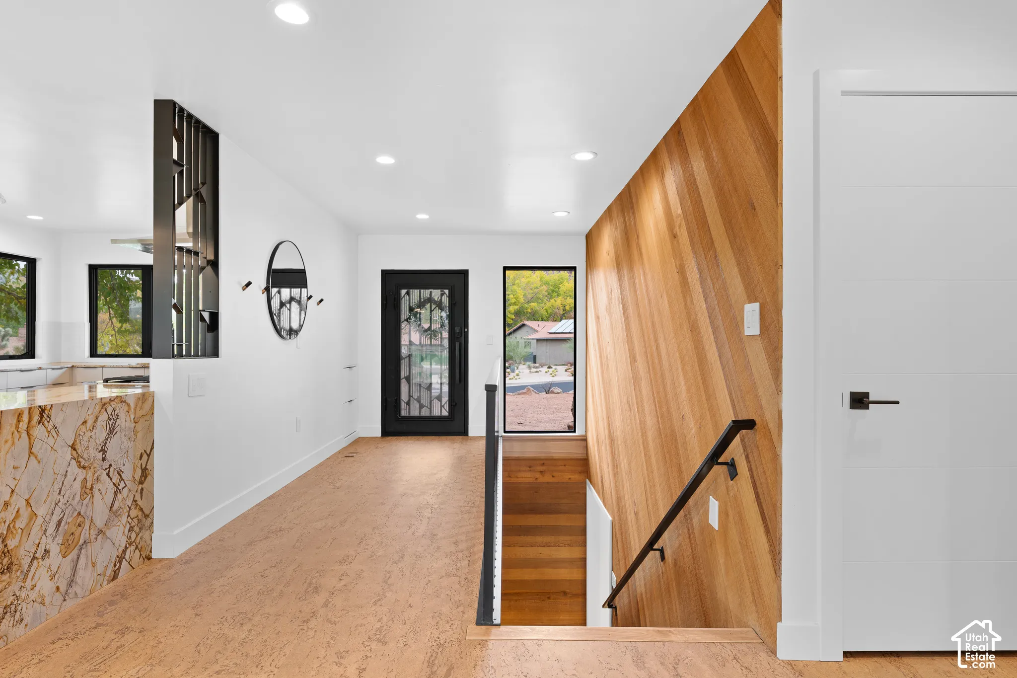 Entryway featuring a decorative wrought-iron front door, cork-finish flooring, a wood-paneled accent wall, and a staircase with a black metal railing