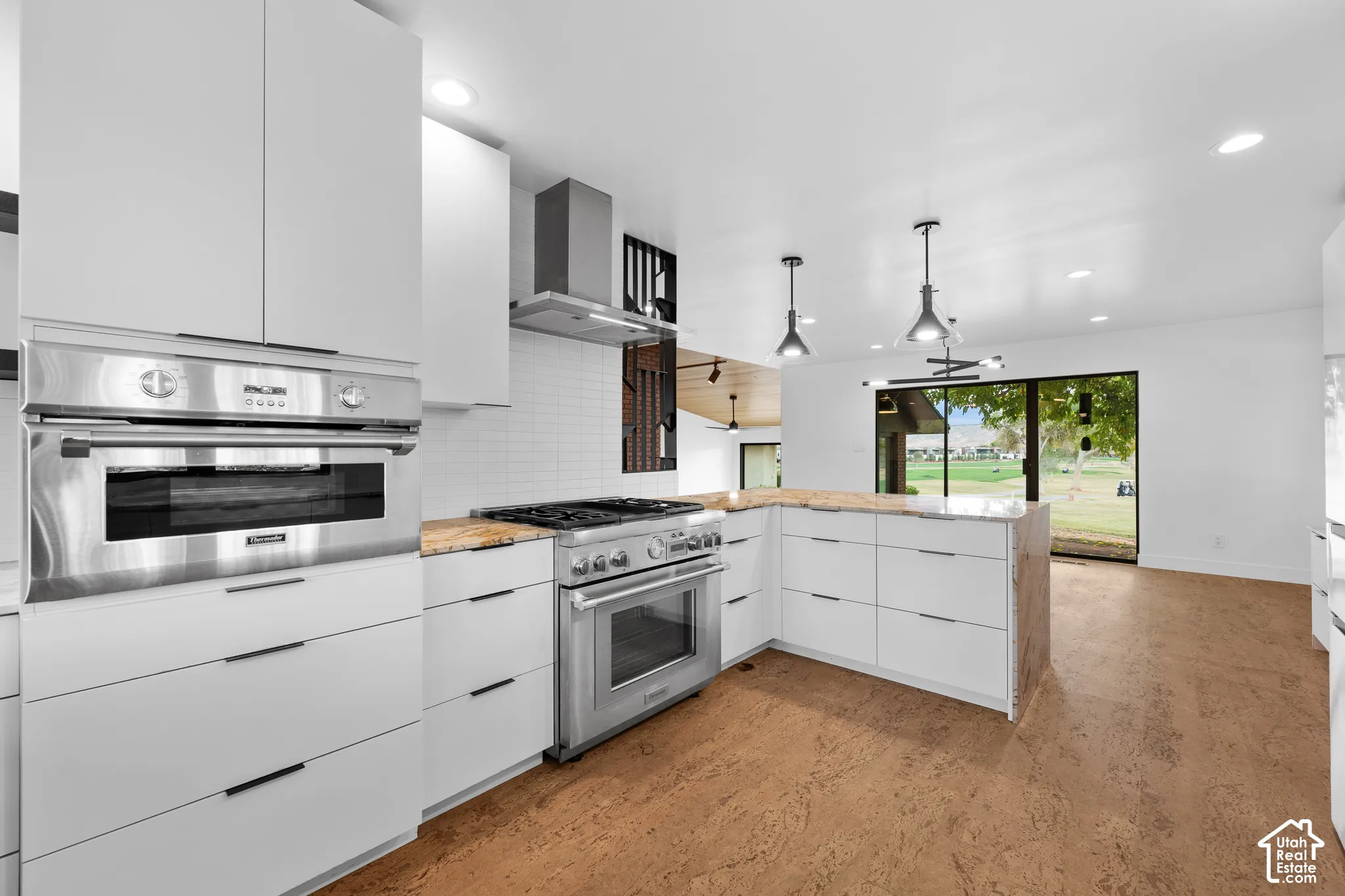 Modern kitchen featuring stainless steel appliances, white flat-panel cabinetry, light-toned countertops, and wood-finish flooring