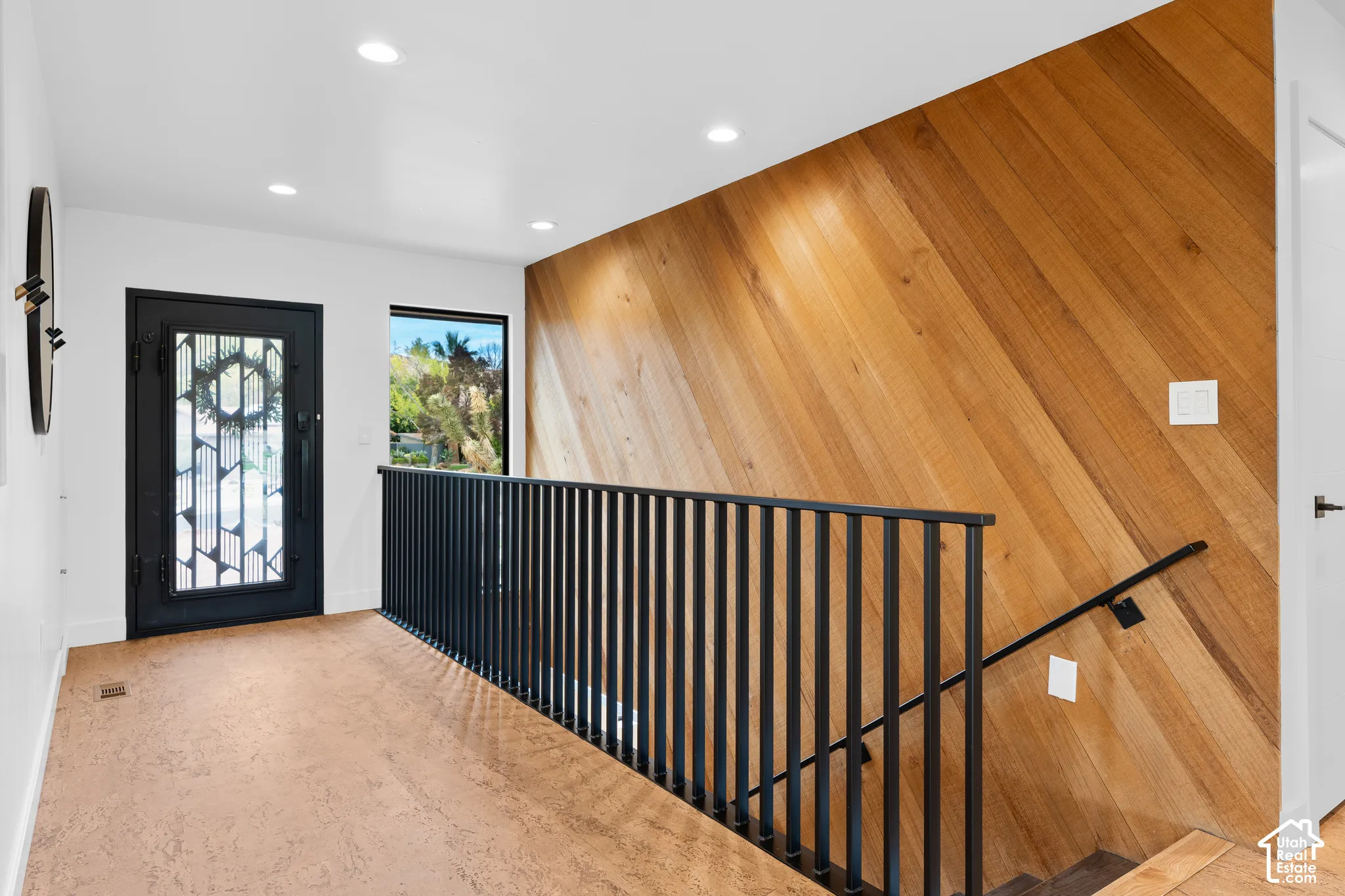Entryway featuring a decorative glass and wrought iron front door, recessed lighting, wood-finish flooring, a diagonal wood accent wall, and a metal spindle railing