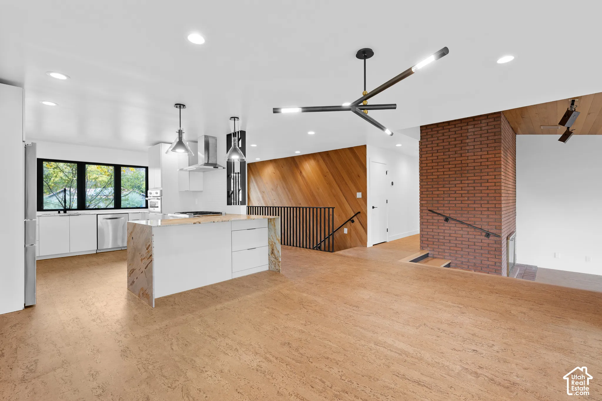 Wood-finish flooring, white cabinetry, stainless steel appliances, brick accent wall, and wood paneling