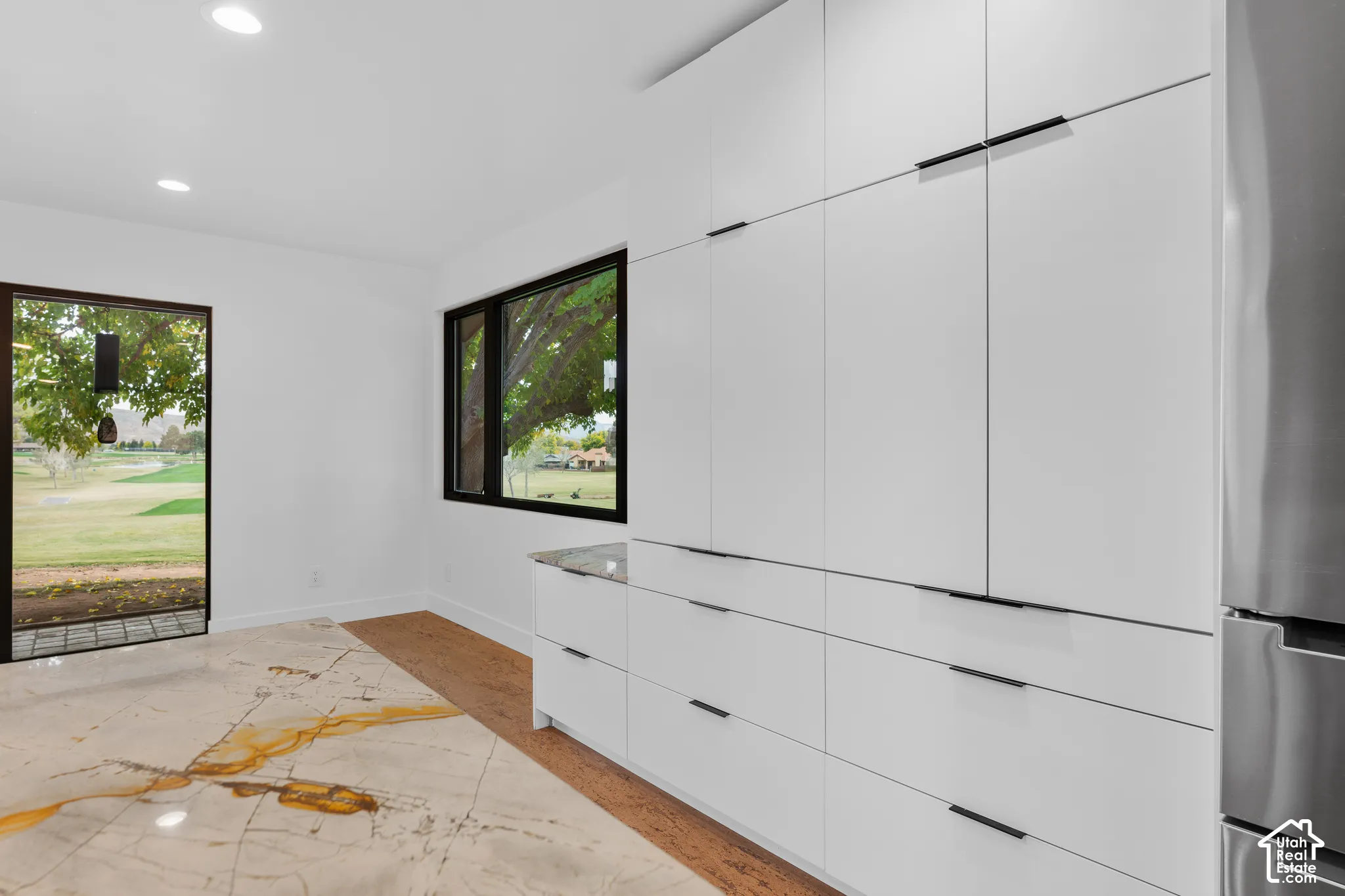 Integrated white cabinetry with matte black hardware, stainless steel refrigerator, stone countertop, recessed lighting, and large format tile flooring