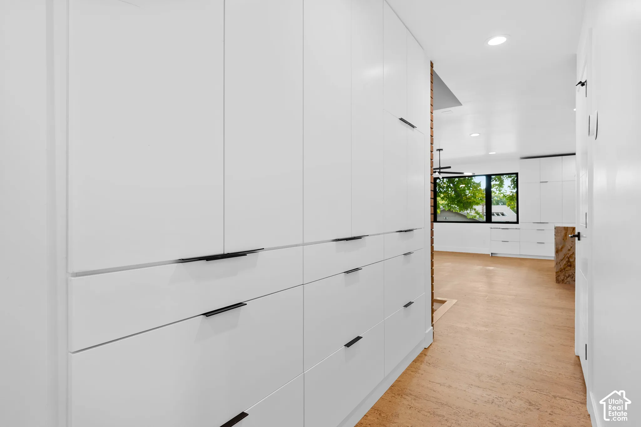 Built-in white flat-panel cabinetry with integrated black pulls, natural cork flooring, recessed lighting, and a large black-framed window