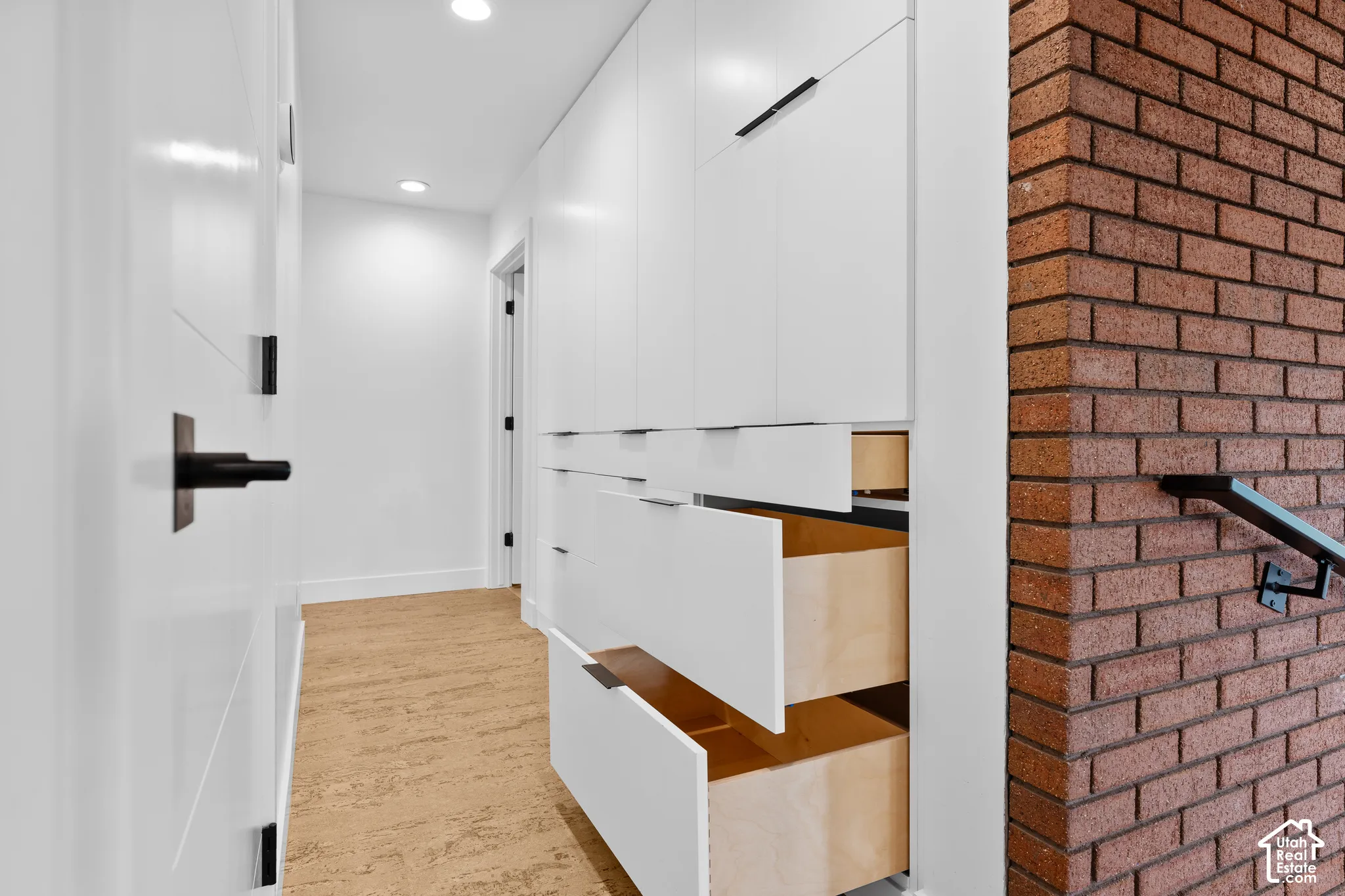 Recessed lighting illuminates the hallway with white flat-panel cabinetry, integrated drawers, and a textured flooring