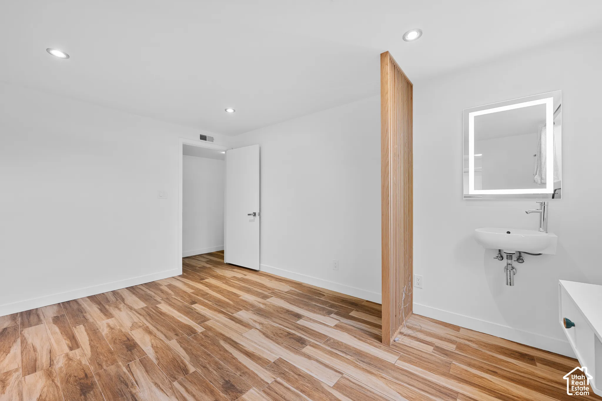 Recessed lighting, wood-finish flooring, and a modern wall-mounted sink with an illuminated mirror