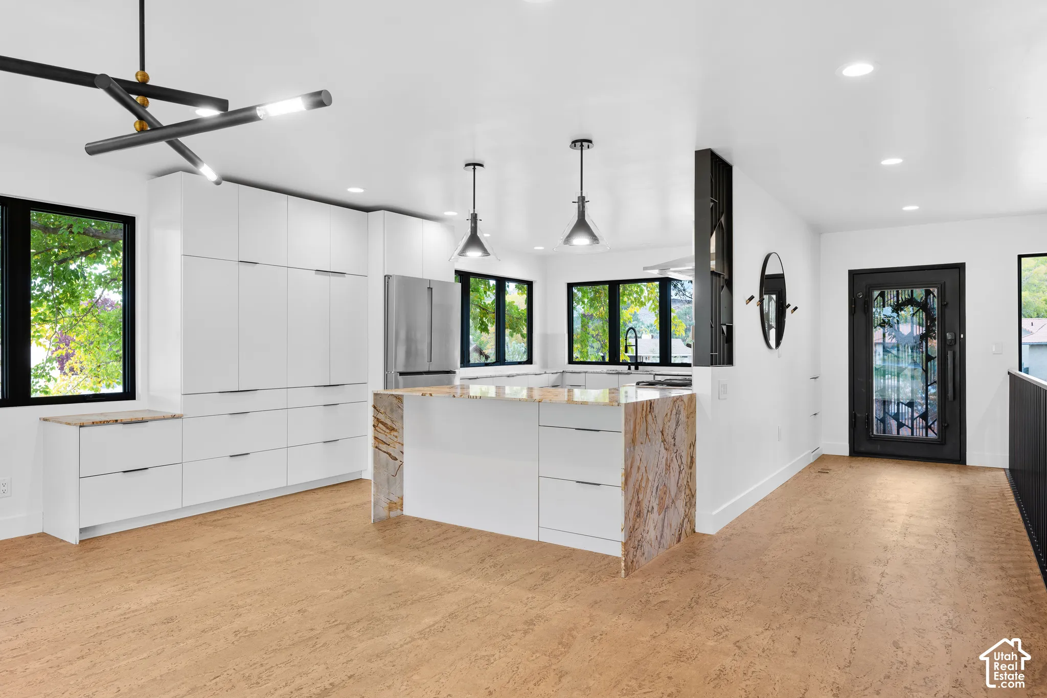 Modern kitchen featuring integrated white cabinetry, a large kitchen island with a waterfall countertop, stainless steel refrigerator, and wood-finish flooring