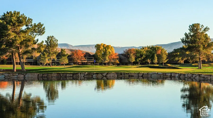 Lakeside setting with a stone retaining wall, expansive green space, mature trees, and distant natural terrain
