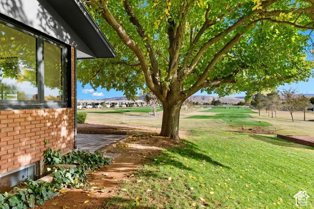 Brick exterior with large windows, mature tree, paved patio area, and expansive green landscape