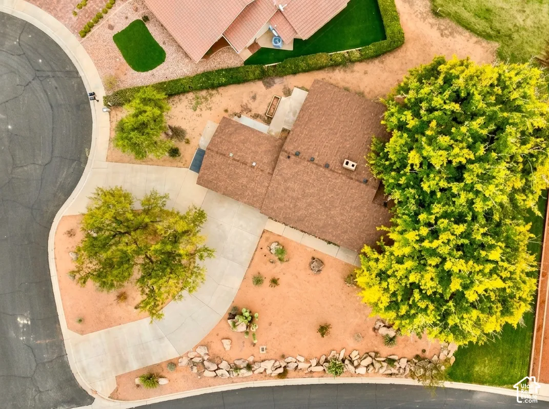 Paved driveway, mature trees, brown shingle roof, desert landscaping, and rock border