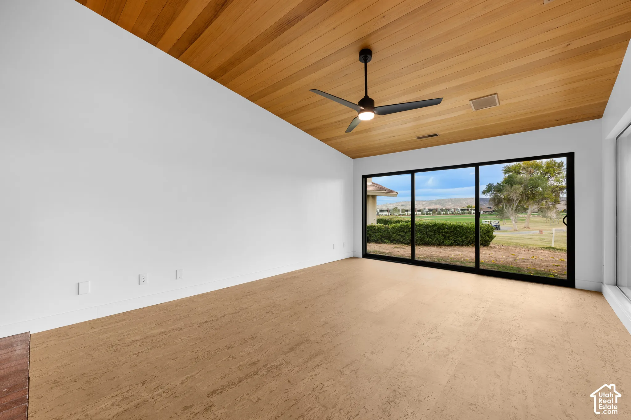 Pitched wood-panel ceiling with a contemporary ceiling fan, large sliding glass doors, and light-toned flooring