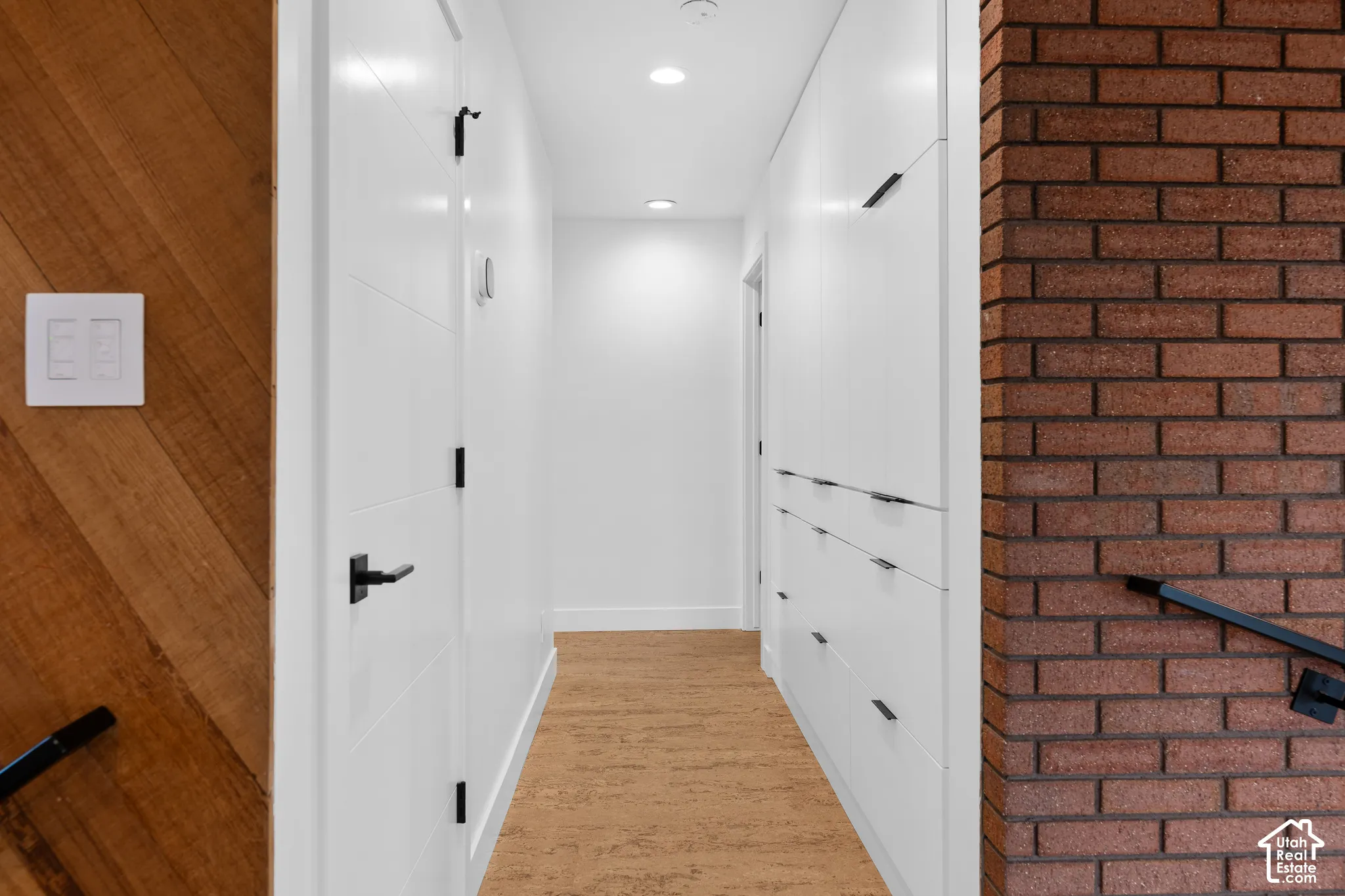 Hallway featuring built-in white cabinetry, cork flooring, recessed lighting, and a brick wall accent