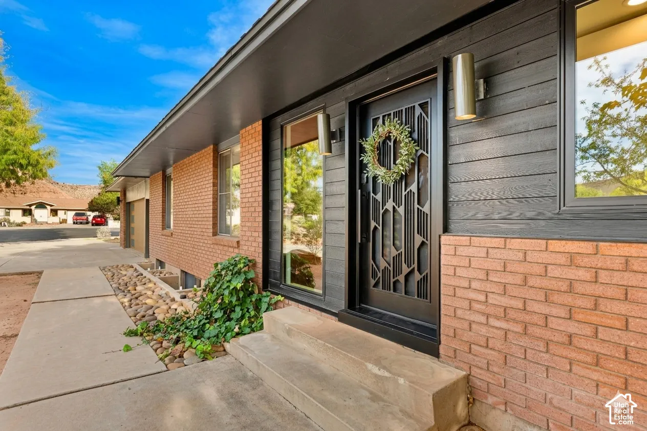 Brick exterior with black horizontal siding, concrete walkway, and a decorative front door