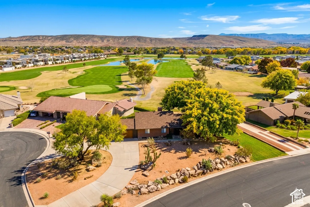 Property with a circular driveway and desert landscaping, situated alongside a manicured golf course with water features and distant mountains