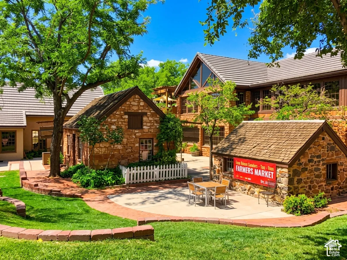 Stone-clad outbuildings with shingle roofs, brick-edged landscaping, mature trees, and a paved patio area