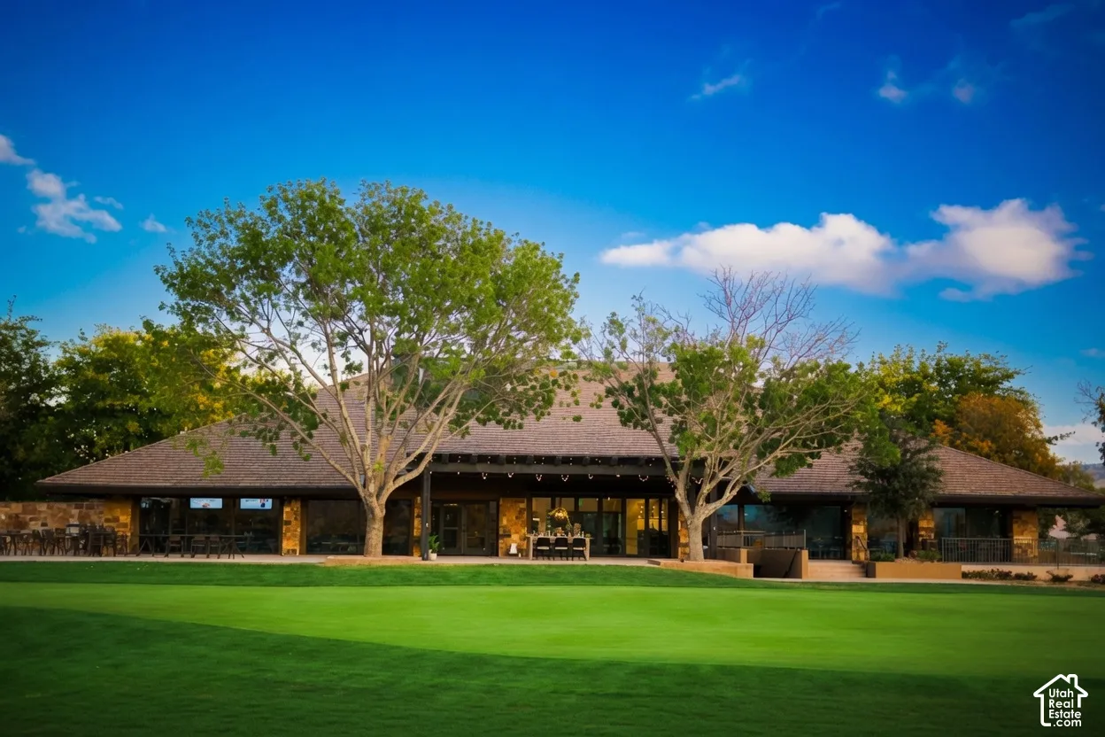 Expansive green lawn, mature trees, single-story building with stone facade, dark-toned roof, and large glass doors