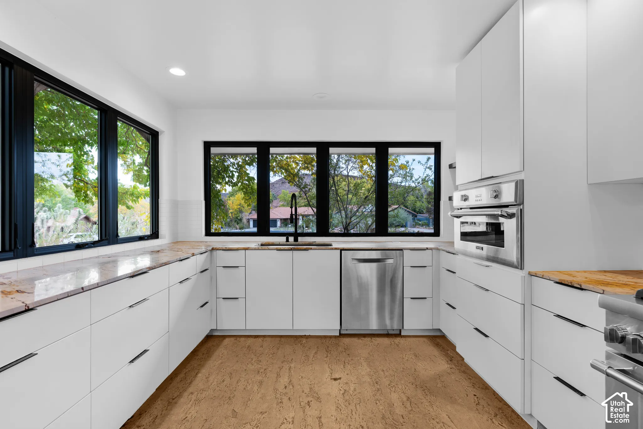 Contemporary kitchen featuring a U-shaped layout, light-toned countertops, white flat-panel cabinetry, stainless steel appliances, and wood-finish flooring
