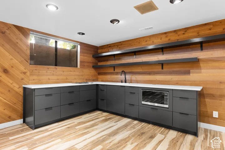 L-shaped lower cabinetry with integrated microwave, white solid surface countertops, a matte black faucet, and wood-finish flooring