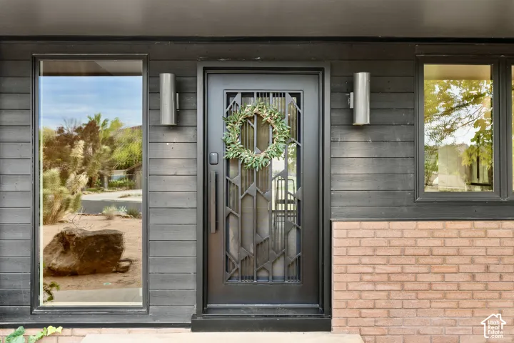 Horizontal wood siding, brick façade, metal entry door with decorative glass, and dual exterior sconce lighting