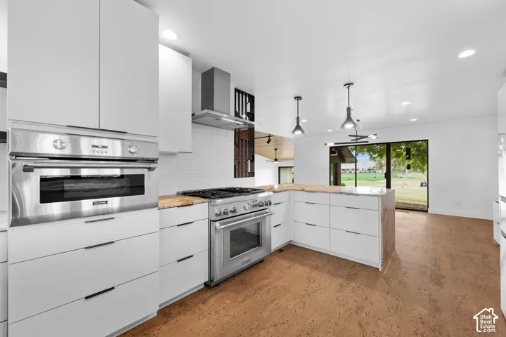 Modern kitchen featuring stainless steel appliances, white flat-panel cabinetry, light-toned countertops, and wood-finish flooring