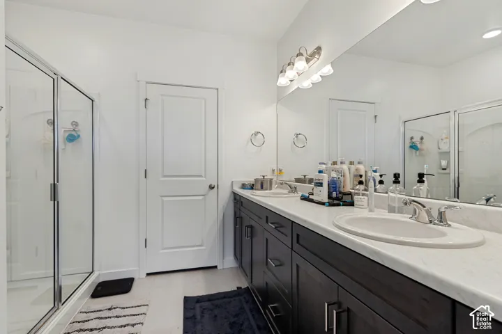 Double vanity with undermount sinks, expansive mirror, dark wood-finish cabinetry, and a glass-enclosed shower