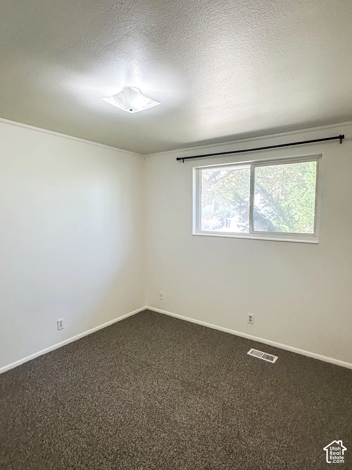 Recessed light fixture, white walls, dark carpet, and a window with a curtain rod
