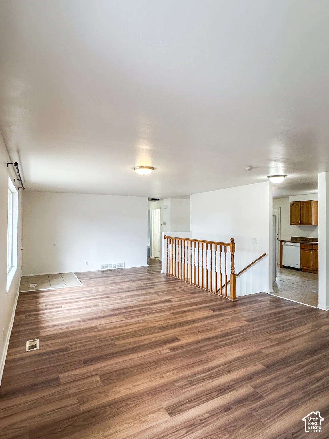 Spacious main living area featuring wood-finish flooring, white walls, and a light wood-finish staircase railing
