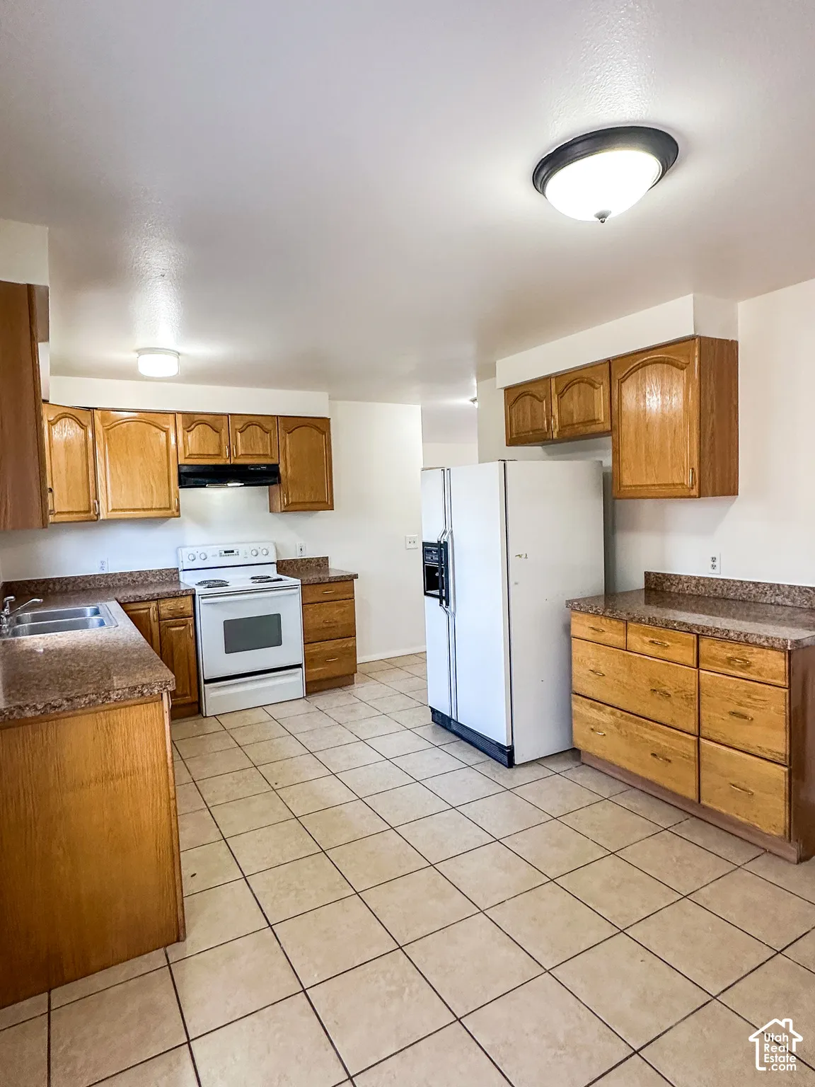 Kitchen featuring wood cabinetry, solid surface countertops, tile flooring, and white appliances