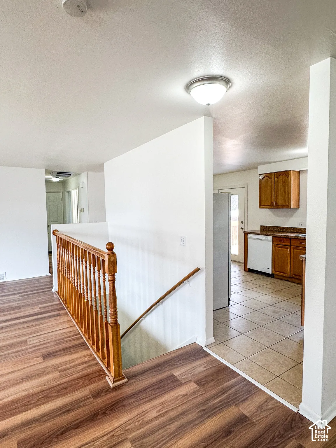 Wood-finish flooring, staircase with wood railing, recessed ceiling light, and kitchen with wood cabinetry and tile flooring