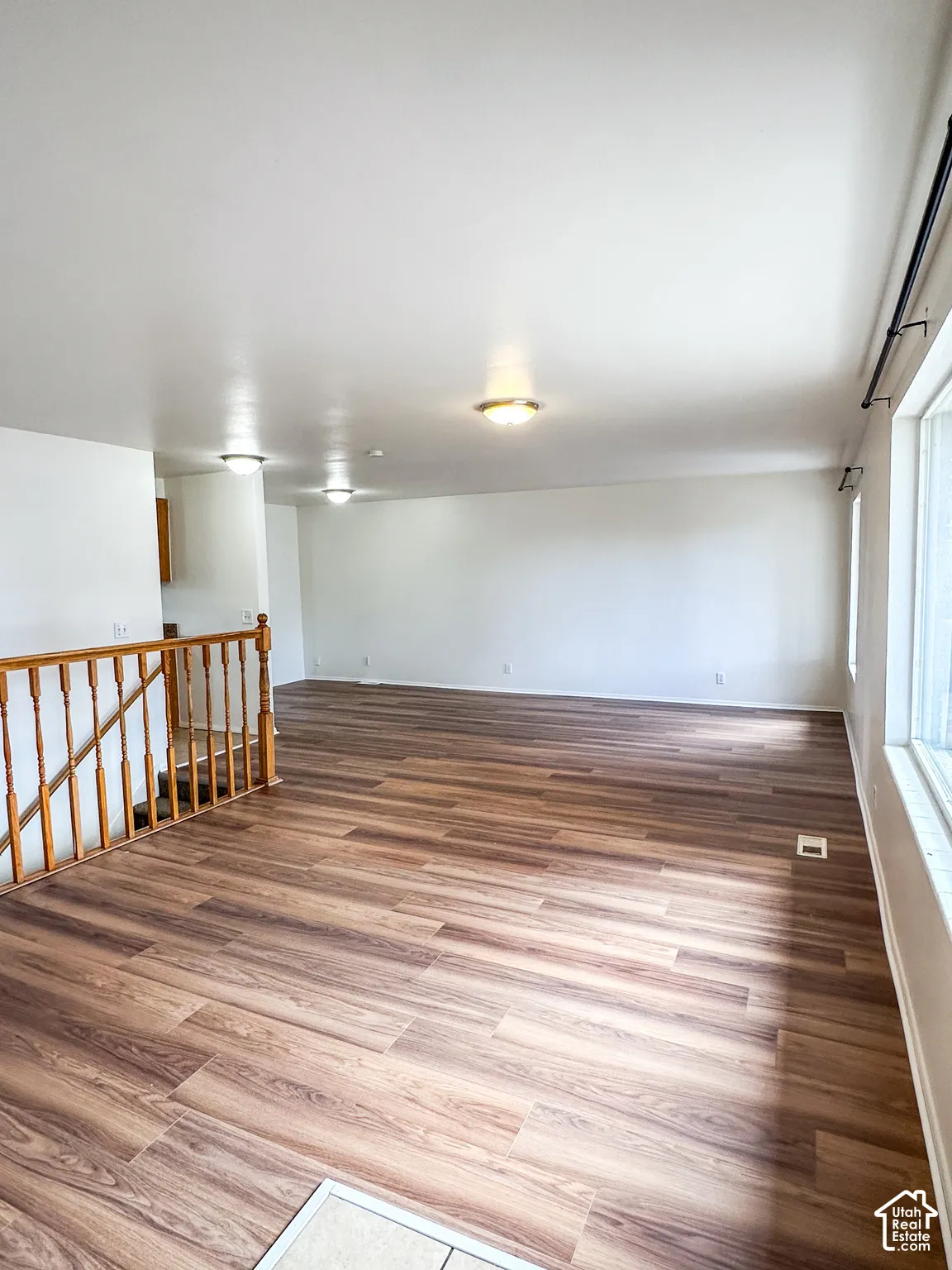 Wood-finish flooring throughout, light neutral wall paint, white trim, and a window with a metal rod