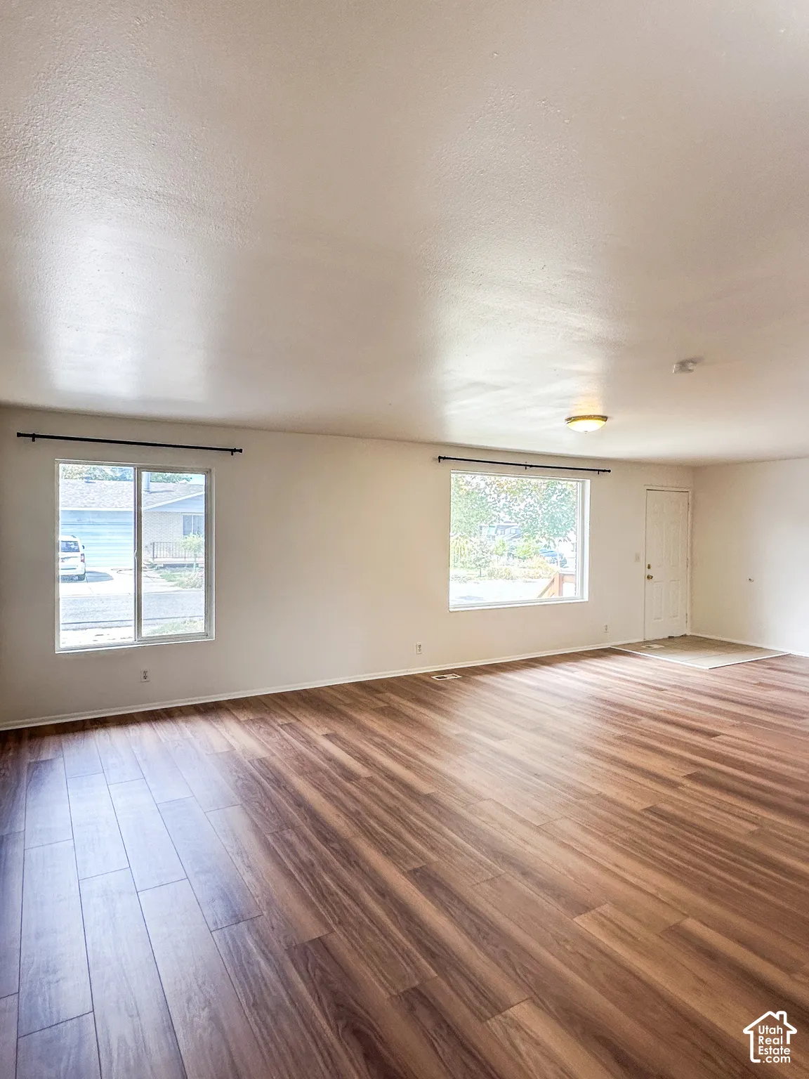 Expansive interior with wood-finish flooring, multiple windows, and a flush-mount ceiling light