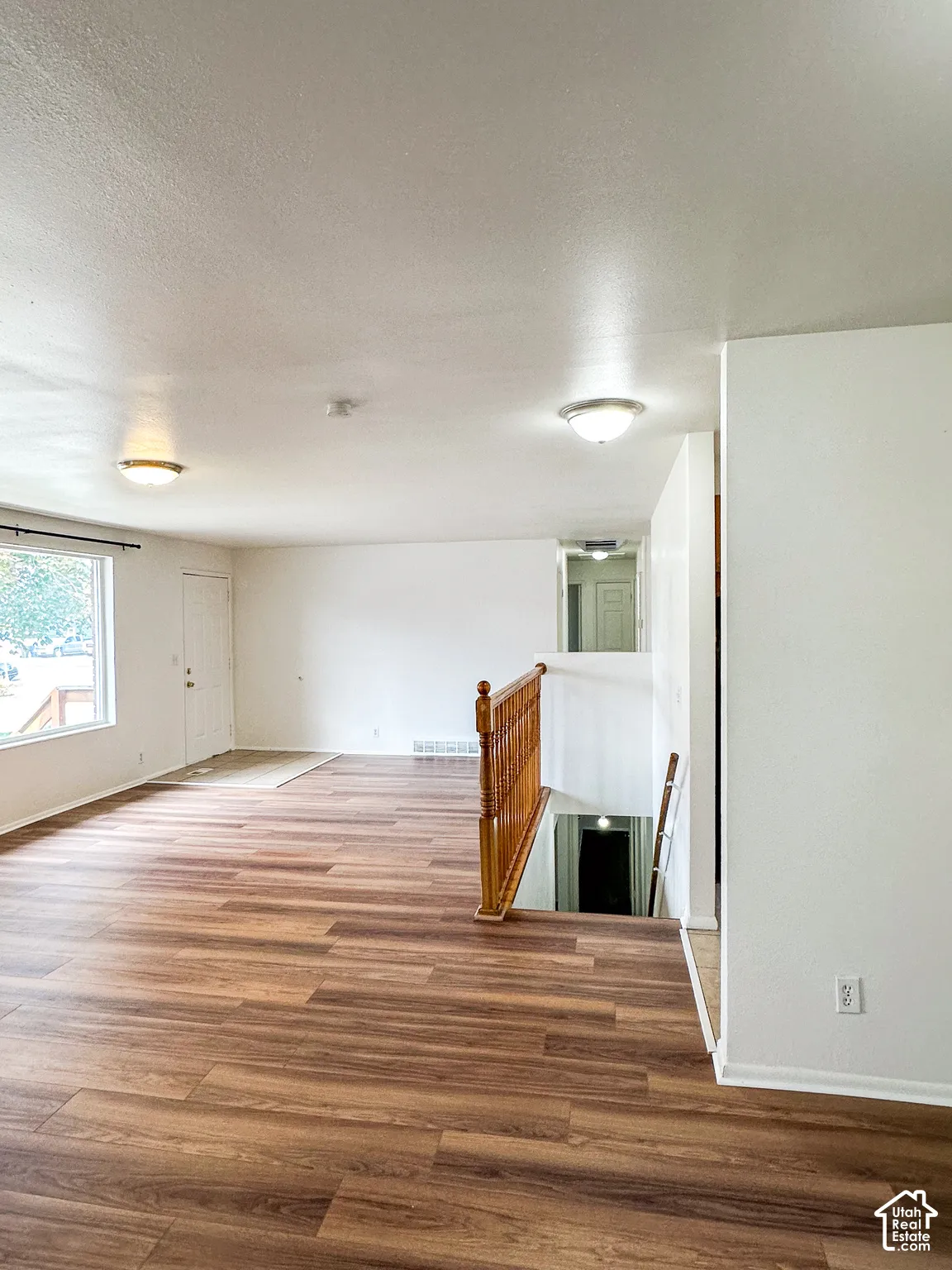 Wood-finish flooring, white walls, flush-mount ceiling lights, and a wood railing