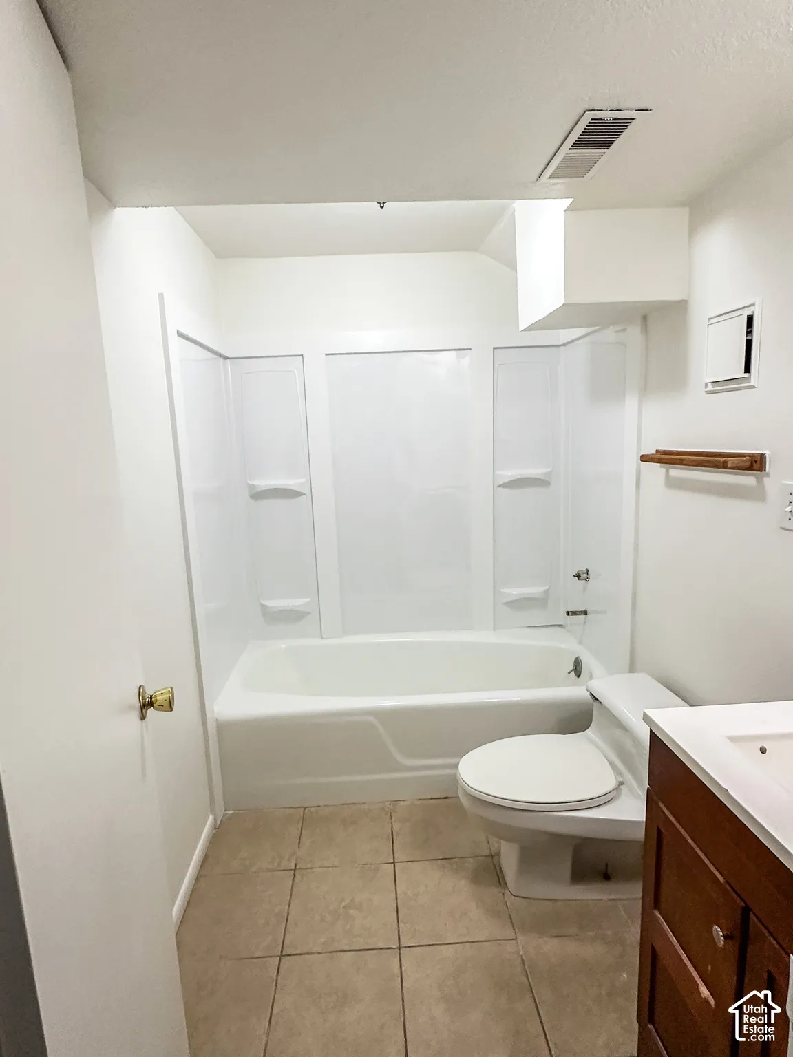 Bathtub with white surround, toilet, wood-finish vanity with white sink, and tiled flooring