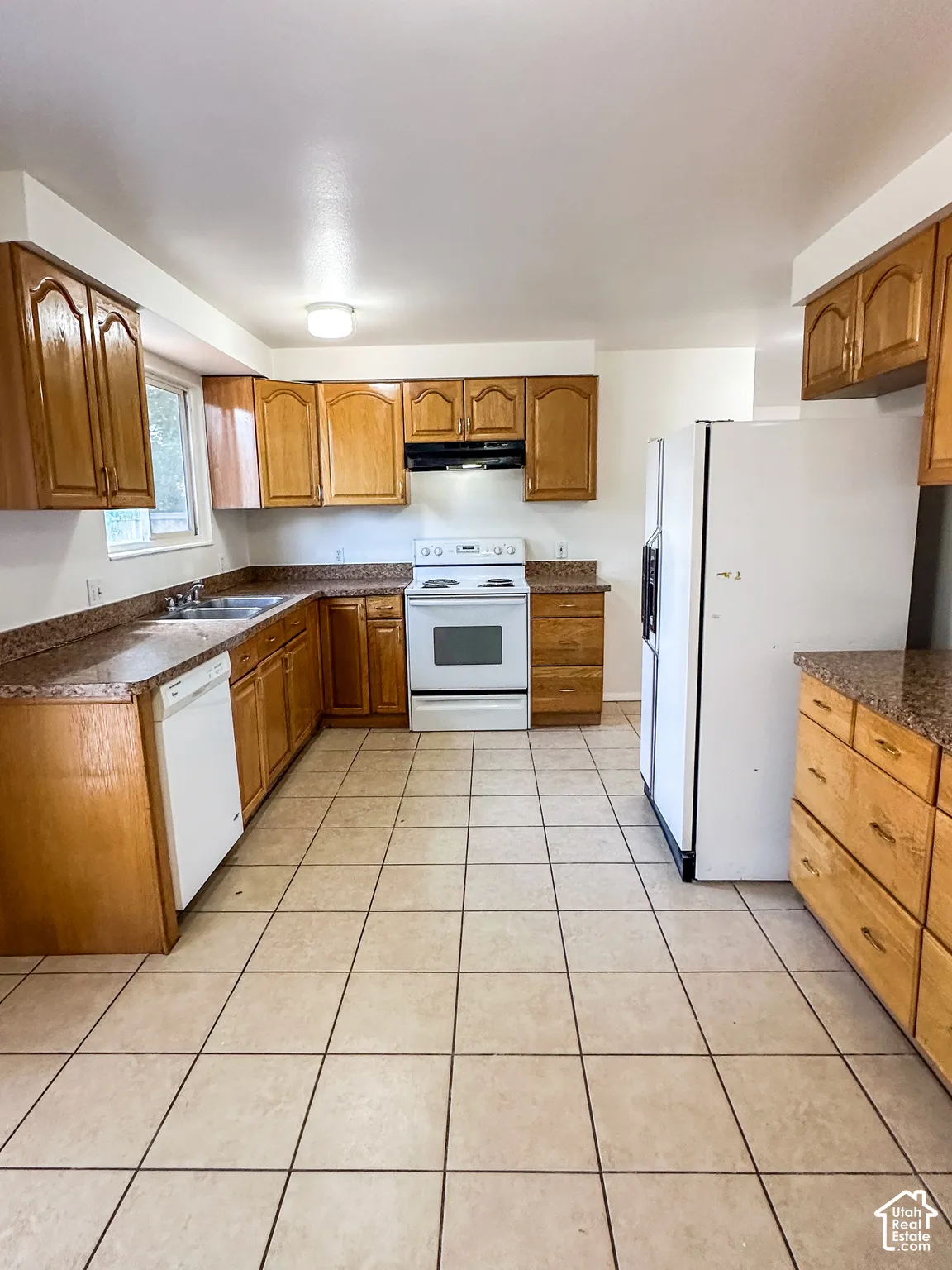 Kitchen featuring wood cabinetry, speckled countertops, tile flooring, and white appliances