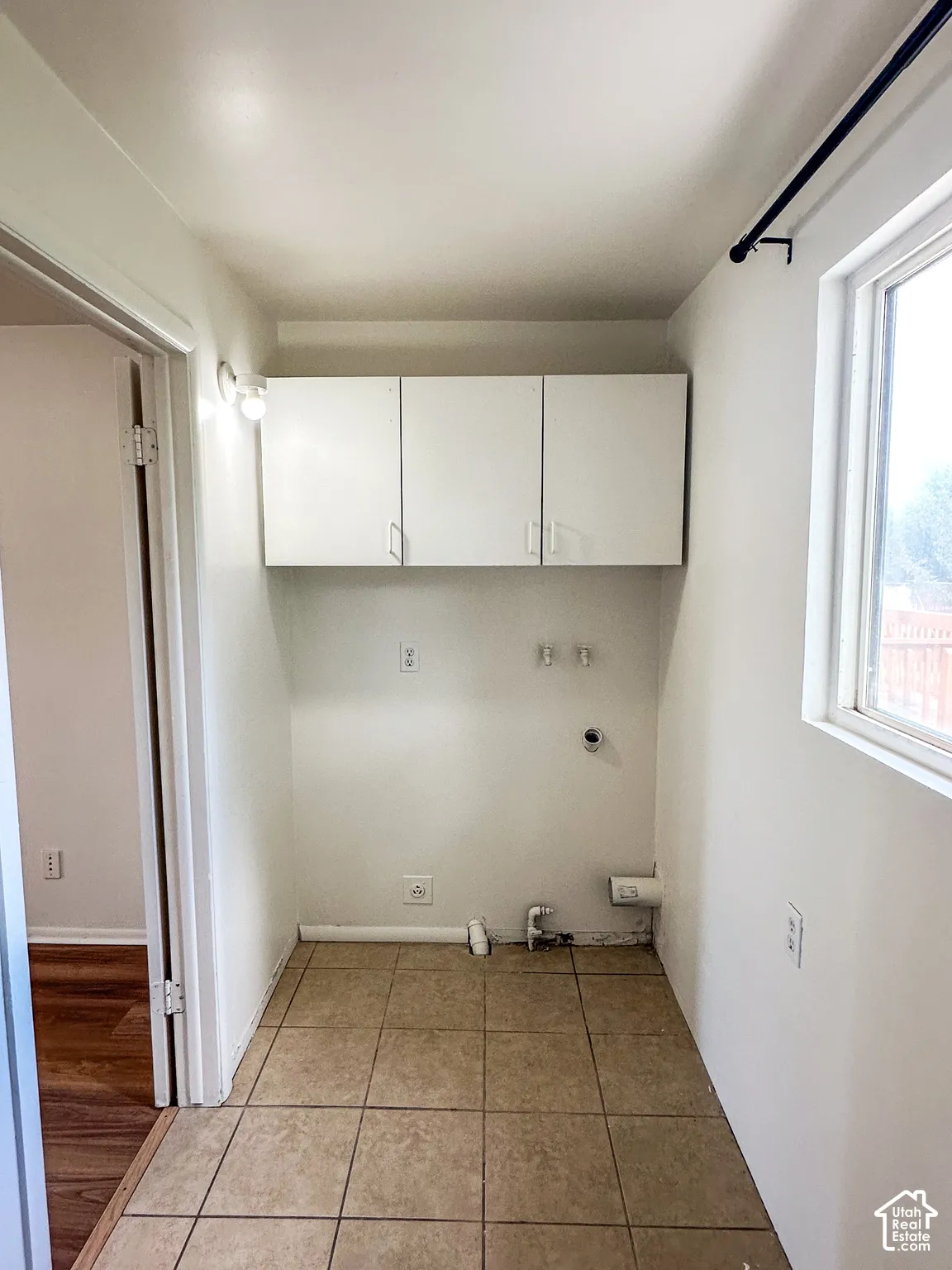Utility area with tiled flooring, upper cabinetry, and a window for natural light