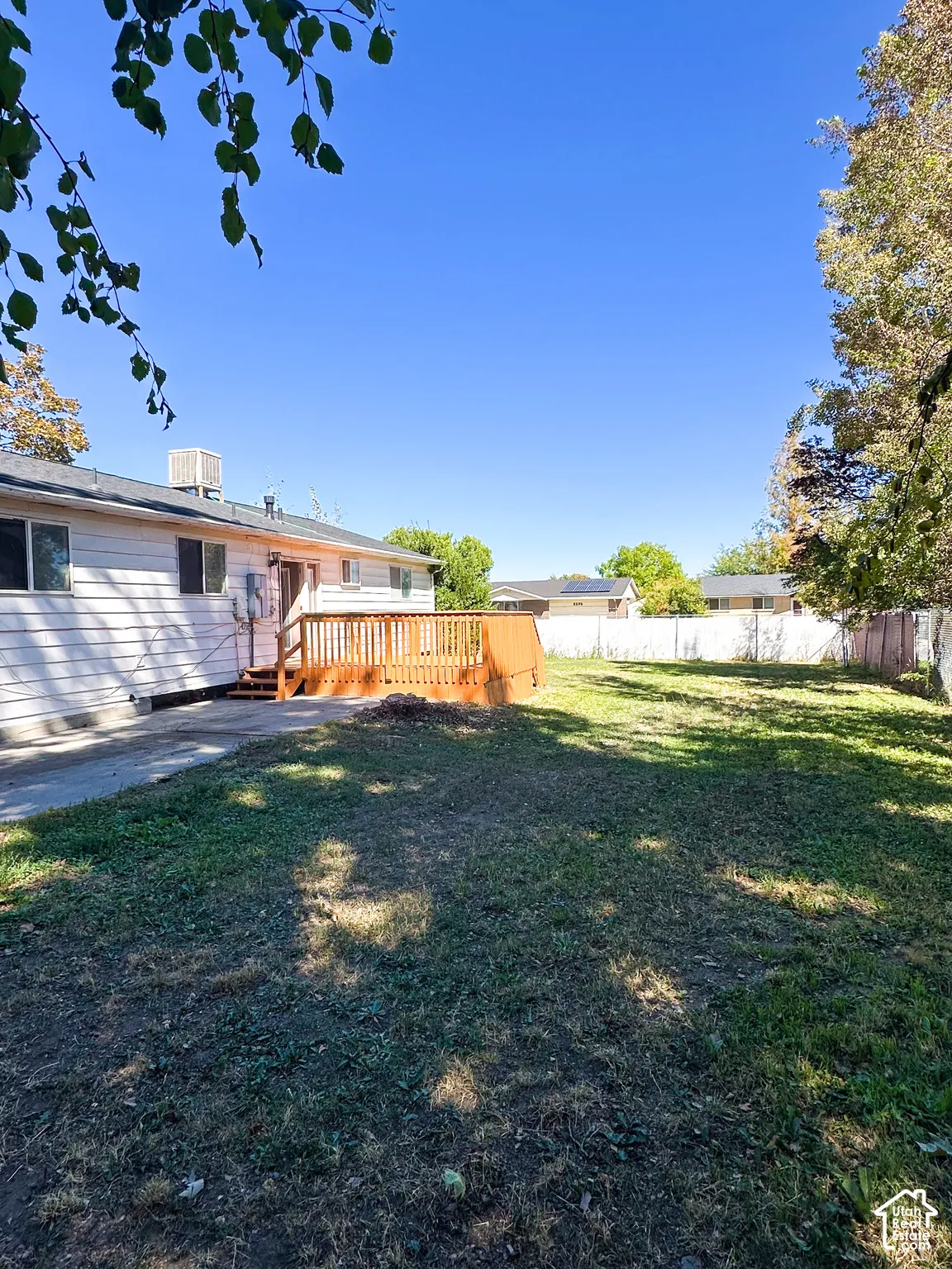Expansive backyard featuring a wood deck, mature trees, and chain-link fencing