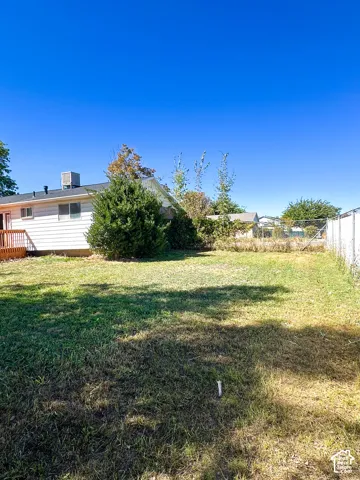 Expansive backyard with a chain-link fence, mature shrubbery, and a wooden deck