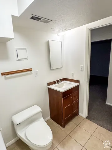 Ceramic tile flooring, white toilet, dark wood-finish vanity with white countertop, integrated sink, and recessed medicine cabinet